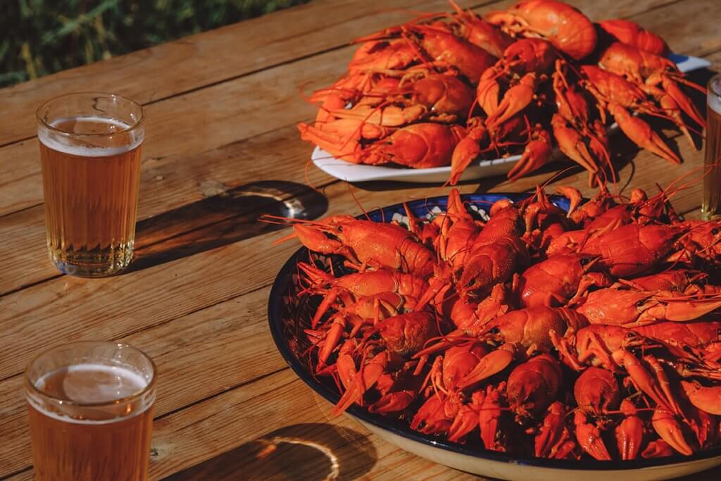 Two big bowls of boiled red crawfish and glasses of beer on wooden table in sunny day