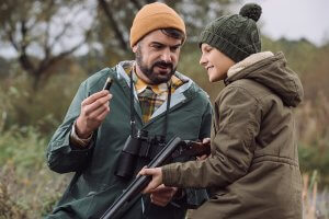A man showing a boy how to put bullet in a gun in the forest
